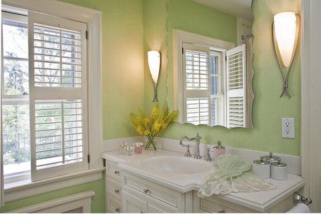 Pink flowers next to green cabinet in bathroom interior with posters and round mirrors